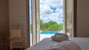 A bedroom with a view of a swimming pool, a wooden chair, and a bed with rolled towels. - Puglia Salento luxury villa with swimming pool and hydro spa. a few km from leuca  (alessano)