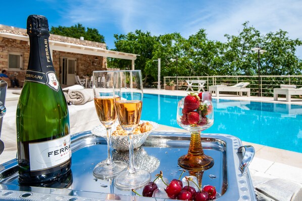 A bottle of Ferrari Brut champagne, two glasses, a bowl of strawberries, and ice cubes on a tray by a pool.