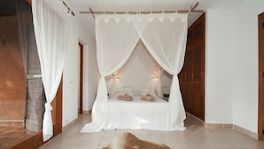A bedroom with a canopy bed, a wooden door, and a large rug. - Cana Lúa. Charming Villa With Fantastic Sea View And Sunset (Sant Josep de sa Talaia)