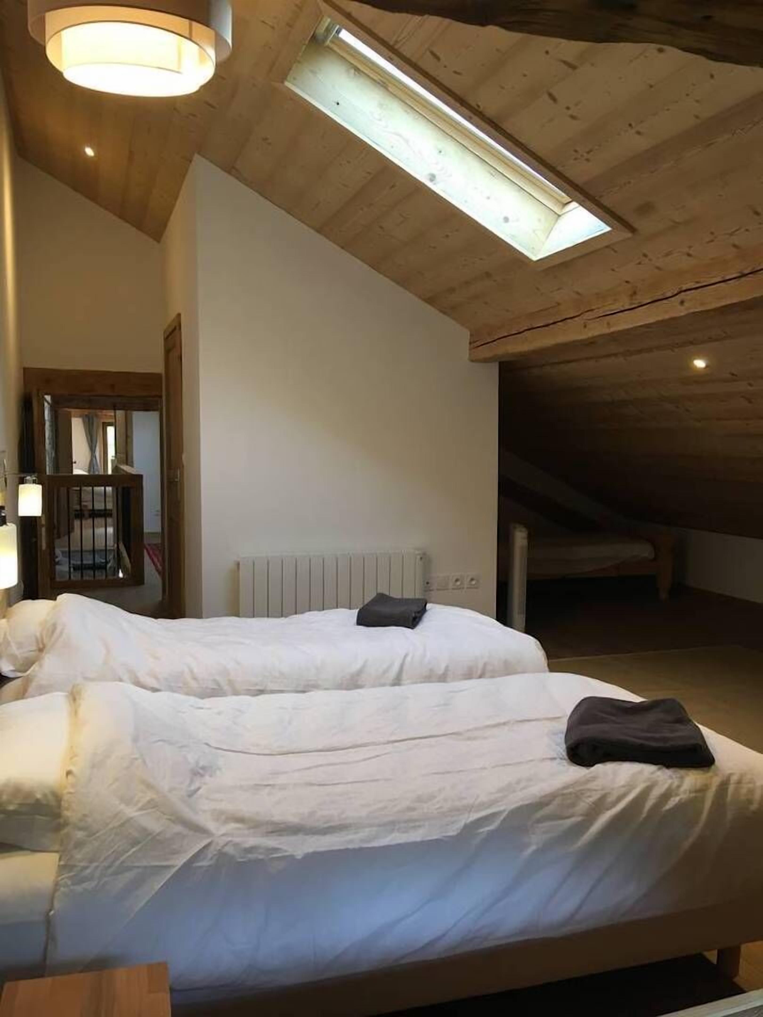 A bedroom with two beds, a skylight, a radiator, and wooden ceiling beams.