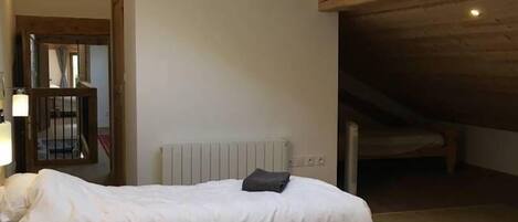 A bedroom with two beds, a skylight, a radiator, and wooden ceiling beams.