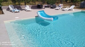 Une piscine équipée de matelas gonflables, de chaises longues et de parasols.