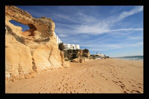 A beach with a large rock formation and a building on a cliff.