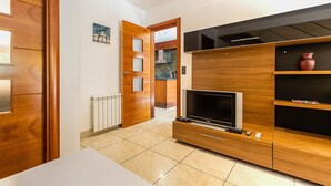 Ein modernes Wohnzimmer mit einer Holz-TV-Konsole, einem Flachbildfernseher und einem durchgehenden Durchgang zur Küche.