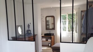 Une chambre avec un grand miroir, un lit, une commode et une fenêtre donnant sur un paysage verdoyant.