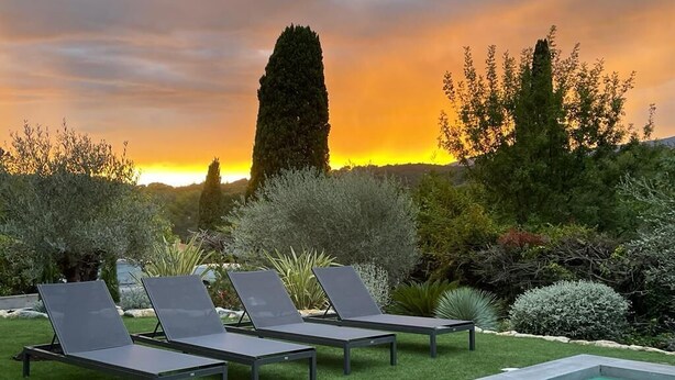 Un espace aménagé au bord de la piscine, avec des chaises longues et une vue sur le coucher du soleil.
