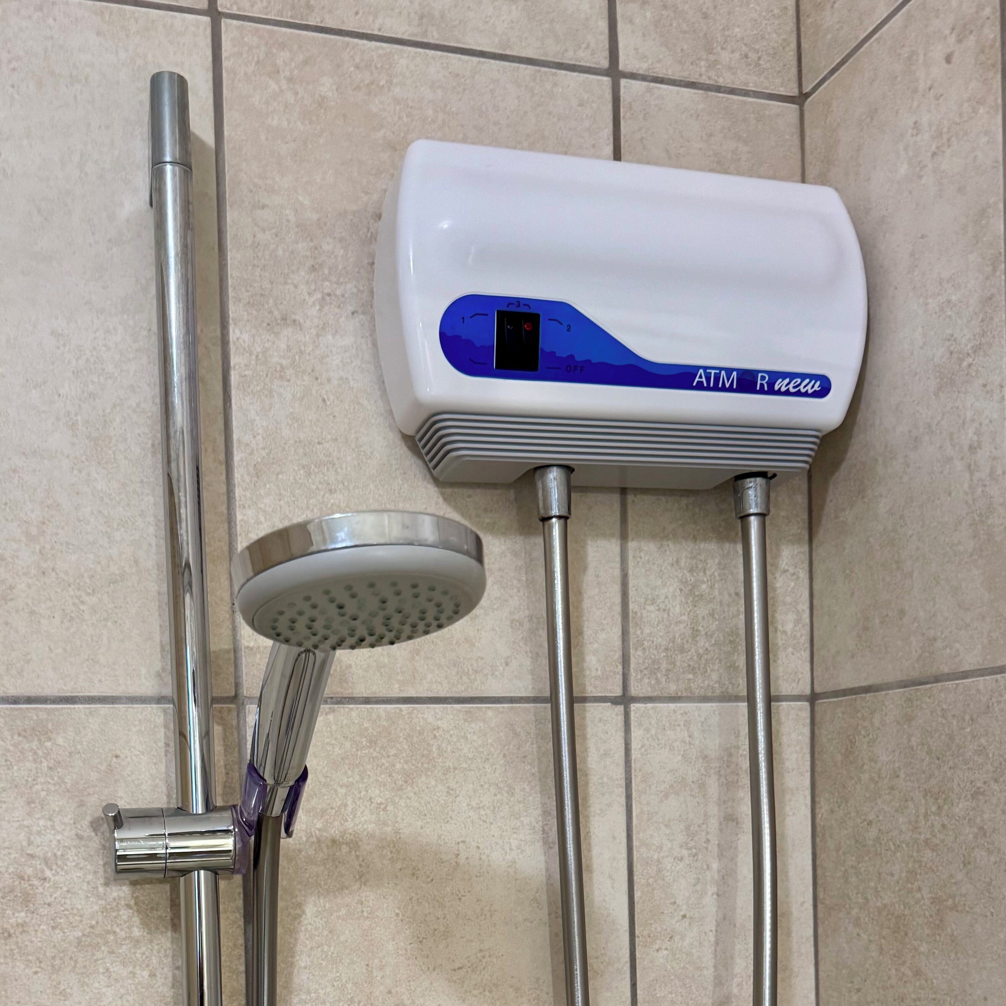 Een badkamer met een witte douchekop, een handdouche en een bedieningspaneel aan de muur met de tekst 'ATM new'.