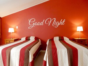 Habitación de hotel con dos camas, cada una con una colcha a rayas, y una pared con el texto 'Good Night'.