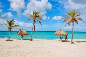 Une plage avec quatre palmiers, un parasol en chaume et un ciel bleu azur.