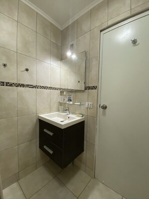 Un baño con lavamanos blanco, mueble oscuro y paredes de azulejos.