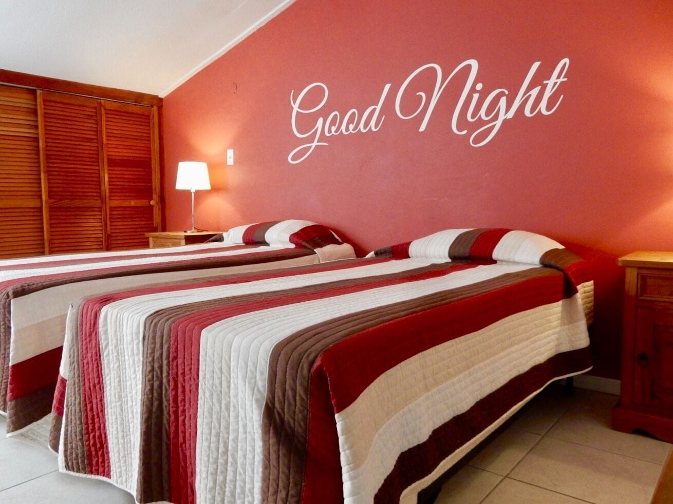 Une chambre d’hôtel avec deux lits, un mur rouge et une pancarte indiquant « Bonne nuit ».