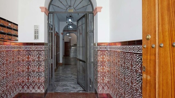 Un couloir aux murs ornés de motifs, une porte en bois et un escalier menant à un autre espace.