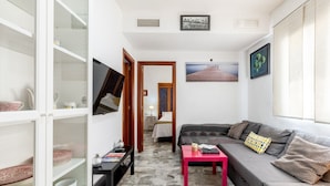Un espace de vie compact comprenant un canapé, une petite table, un téléviseur fixé au mur et une bibliothèque.