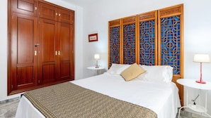 Une chambre d’hôtel dotée d’une grande armoire en bois, d’un lit avec du linge de lit blanc, d’une tête de lit décorative et de deux tables de chevet avec des lampes.