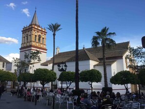 A plaza with a church and a bell tower, surrounded by palm trees and outdoor seating. - El Rico Rincón in Sanlúcar la Mayor (22 km from Seville) (Sanlúcar la Mayor)