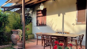 A patio with a wooden table and chairs, surrounded by potted plants and a yellow wall.