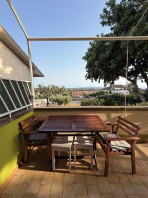 An outdoor patio with a wooden table and benches, a view of the countryside, and a green wall.