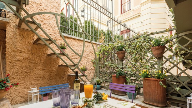 An outdoor patio with a table set for dining, surrounded by potted plants and a metal railing. - Hidden Gem on the Spanish Steps - Terrace - Great Air Conditioning (Roma)