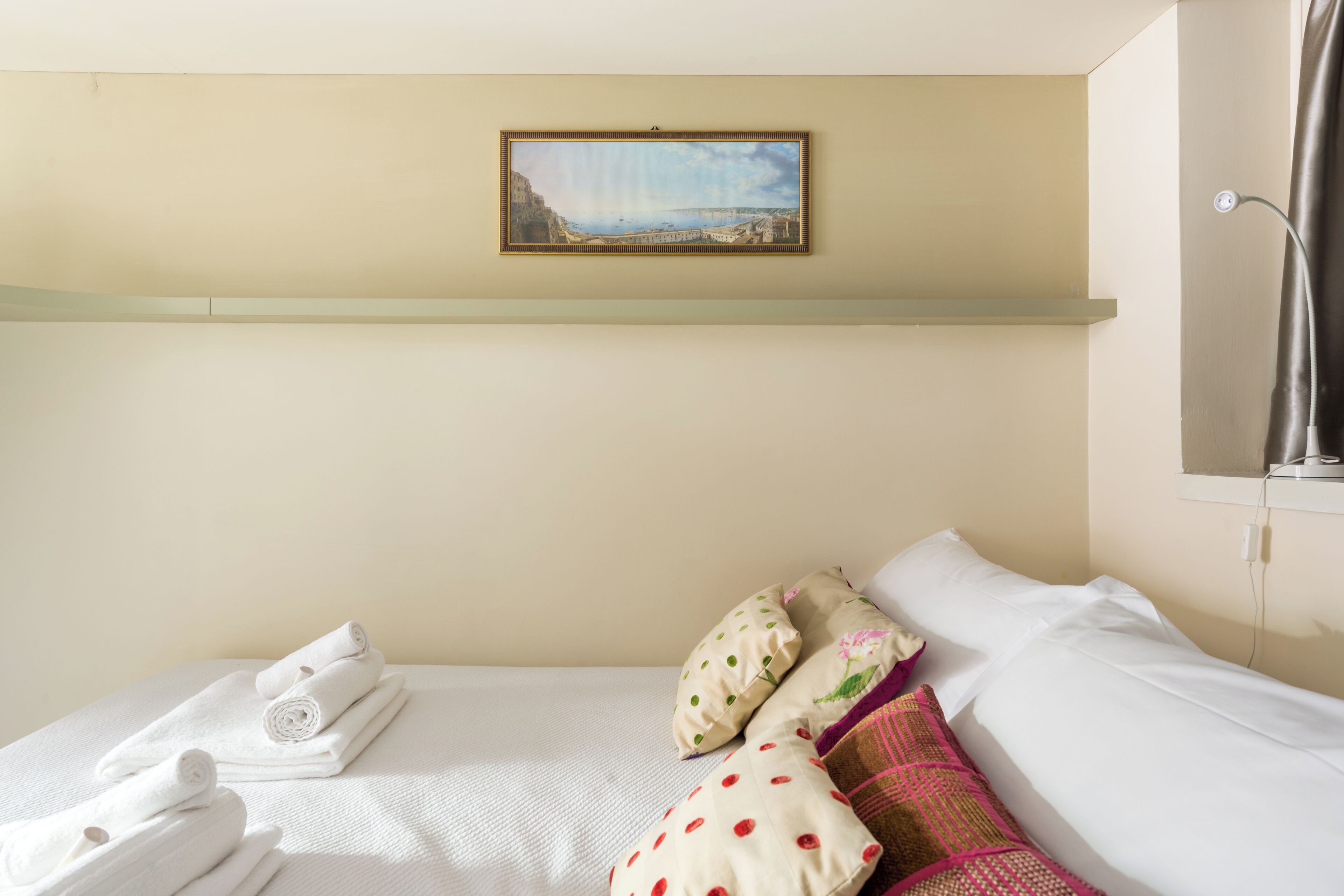 Quarto de hotel com cama, almofadas, um quadro e um porta-toalhas.