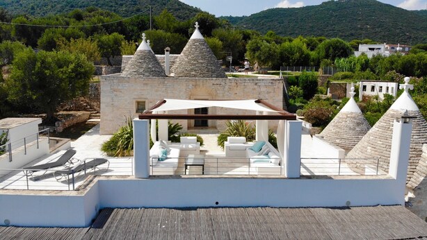 A rooftop terrace with stone-tiled roofs, a stone building with a conical roof, and outdoor seating with umbrellas.