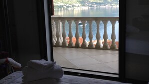 Een hotelkamer met een bed, een raam met uitzicht op bergen en een meer, en een balkon met een hekwerk.