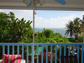 Enjoy the ocean view from this balcony with lush surroundings and a ceiling fan.