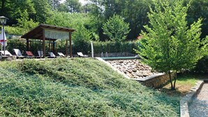 A pool area with lounge chairs, a covered seating area, and a stone wall.