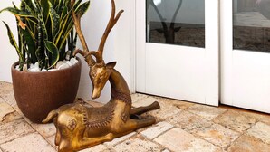 Una planta en maceta con hojas variegadas, una escultura de ciervo de bronce y una puerta de vidrio que refleja una pared de piedra y plantas.