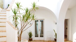 Un interior en tonos blancos con suelo de baldosas, una escalera y plantas en macetas.