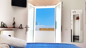 Un dormitorio con cama, televisor en la pared y vista al cielo y edificios a través de una puerta abierta.
