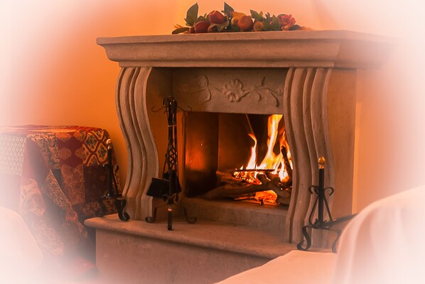 A stone fireplace with a fire burning inside, surrounded by a patterned rug and a chair.