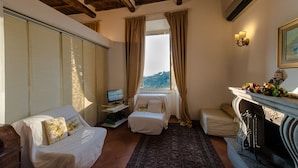 Um quarto acolhedor com teto de madeira, uma cama, uma escrivaninha com computador, lareira e janela com cortinas.