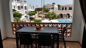 Un balcon avec une table et des chaises, donnant sur une piscine et des bâtiments aux murs blancs et aux toits rouges.