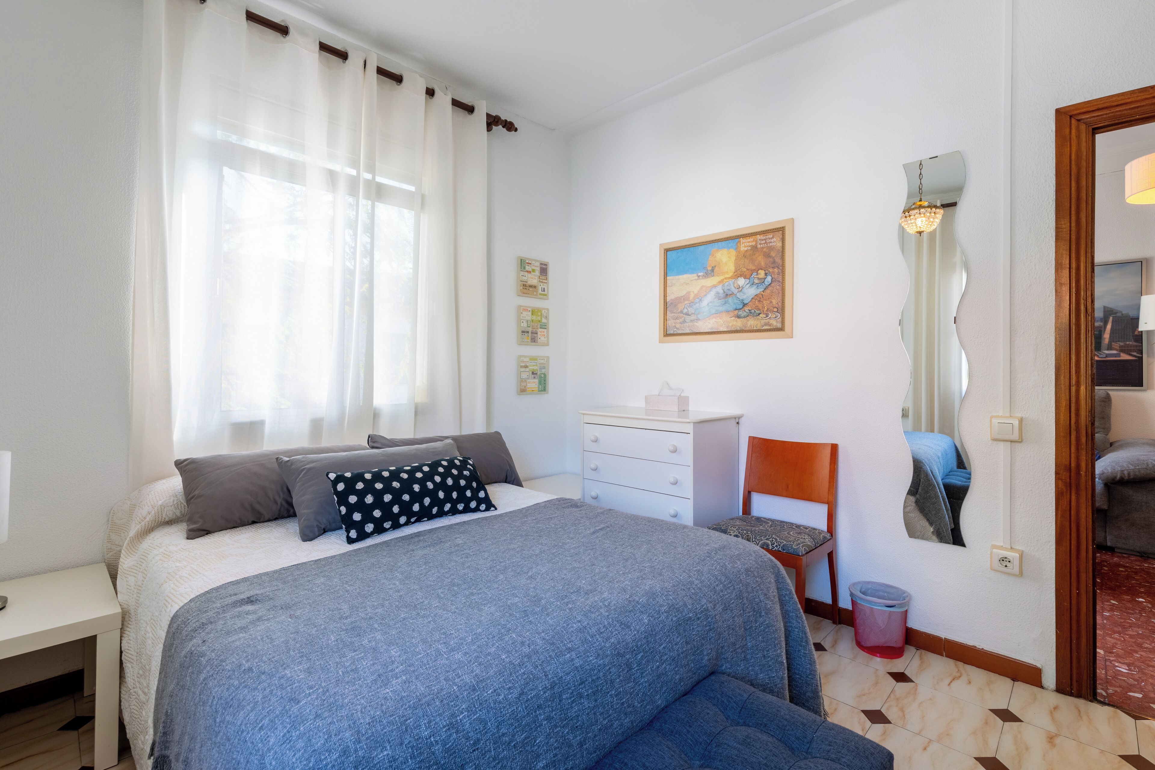 Ein Schlafzimmer mit einem Bett, einem Sessel, einem Schreibtisch, einem Spiegel und einem Bild an der Wand.