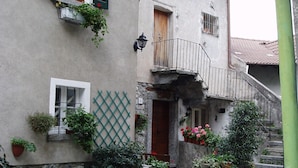 A two-story building with a stone facade, multiple windows with shutters, and a small balcony with a metal railing.