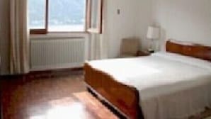 A hotel room with a large window, a bed, a nightstand, and a lamp.