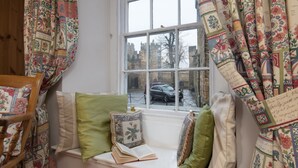 A cozy reading nook with a window seat, patterned curtains, and a view of a historic building. - Barbican View, luxury Grade II listed apartment opposite Alnwick Castle (Alnwick)