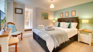 A bedroom with a bed, bedside tables, a chair, a desk, and a bathroom visible through an open door. - Barbican View, luxury Grade II listed apartment opposite Alnwick Castle (Alnwick)