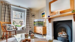 A cozy living room with a fireplace, a wooden chair with a cushion, a television, and a magazine on the coffee table. - Barbican View, luxury Grade II listed apartment opposite Alnwick Castle (Alnwick)