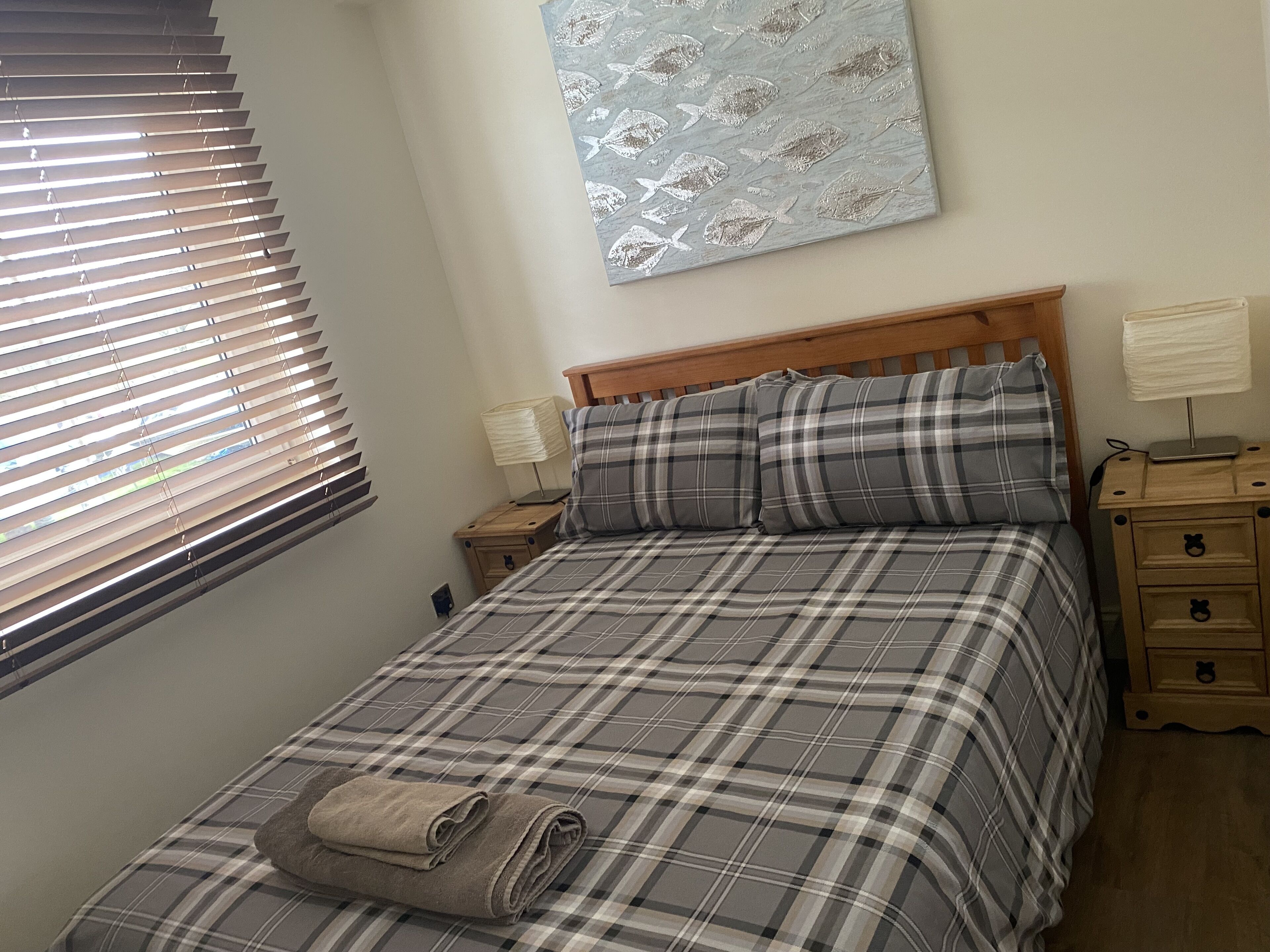 Une chambre à coucher avec un lit, une table de chevet, une lampe et une fenêtre avec des stores.
