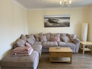 A living room with a sofa, ottoman, coffee table, and a painting of a boat on water.