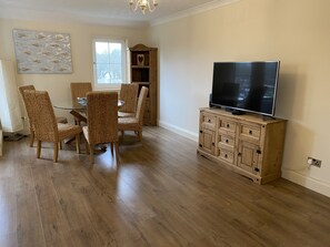 A dining area with wicker chairs, a glass table, and a wooden cabinet with a TV.