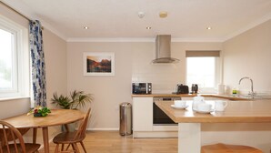 A modern kitchen with a wooden dining table, chairs, a small island with kitchenware, a microwave, a toaster, and a sink. - Spacious 1 bedroomed apartment in the seaside village of Gwithian (Gwithian)