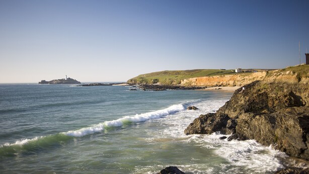 A coastal landscape with rocky shores, a lighthouse, and a grassy hill. - Spacious 1 bedroomed apartment in the seaside village of Gwithian (Gwithian)