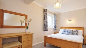 A bedroom with a wooden bed, a nightstand, a dresser, a mirror, and a window with patterned curtains. - Spacious 1 bedroomed apartment in the seaside village of Gwithian (Gwithian)