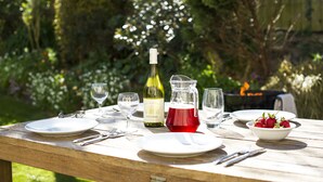 A wooden table set for a meal with plates, cutlery, a wine bottle, a pitcher of red drink, and a bowl of strawberries. - Spacious 1 bedroomed apartment in the seaside village of Gwithian (Gwithian)