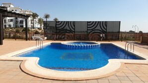 Una piscina con borde de azulejos, rodeada por un suelo de ladrillo y una valla decorativa.