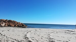 Una playa arenosa con huellas que conducen a un promontorio rocoso.