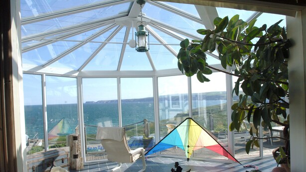 A conservatory with a glass ceiling, a view of the sea, and a chair.