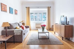 A living room with a sofa, coffee table, TV, and a window with curtains.